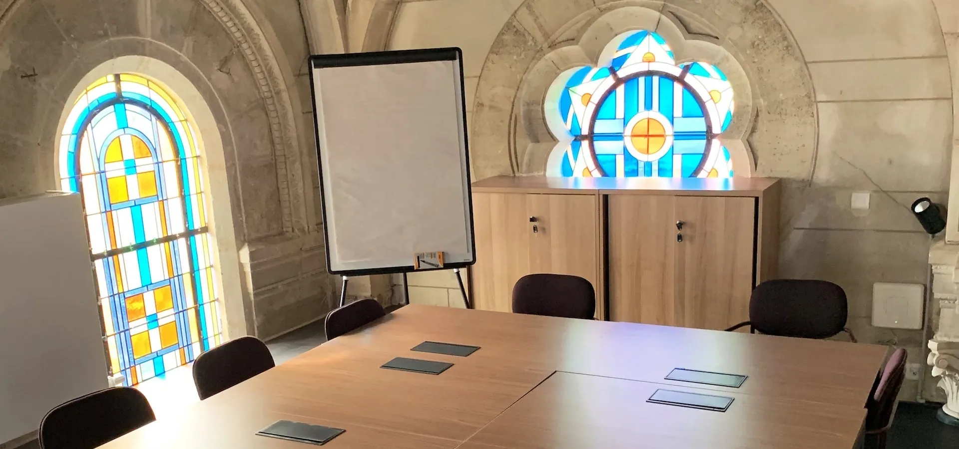 Salle de réunion avec un vitrail en rosace et un paperboard